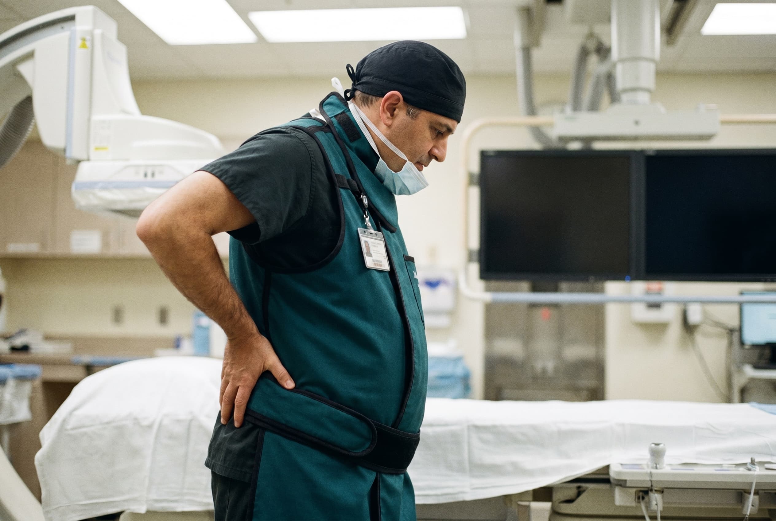 Interventional cardiologist showing lower back strain after a long fluoroscopy case, lead apron still on